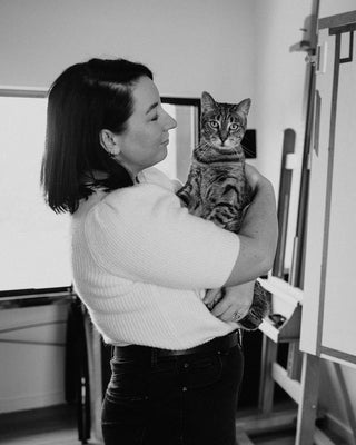 Artist Laura J Stratton holding her cat next to an artwork in her studio.