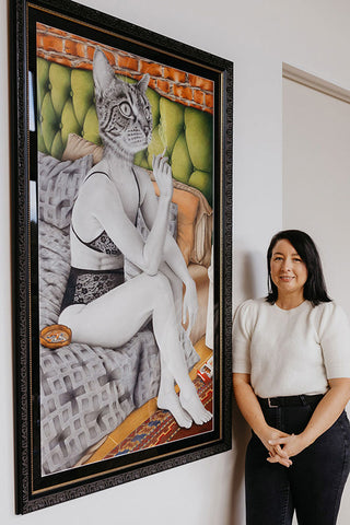 Artist Laura J Stratton standing next to her original artwork Welcoming Tuesday which is framed and hanging on a wall.