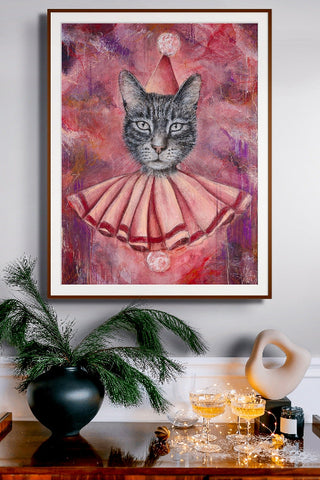 Framed artwork of a cat in a party hat and dress on a wall above a table with drinks and decor.